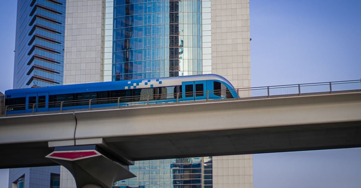 Dubai Travel Guide: Getting Around and Eating Well A sleek metro train passes high above a modern cityscape with tall glass skyscrapers.