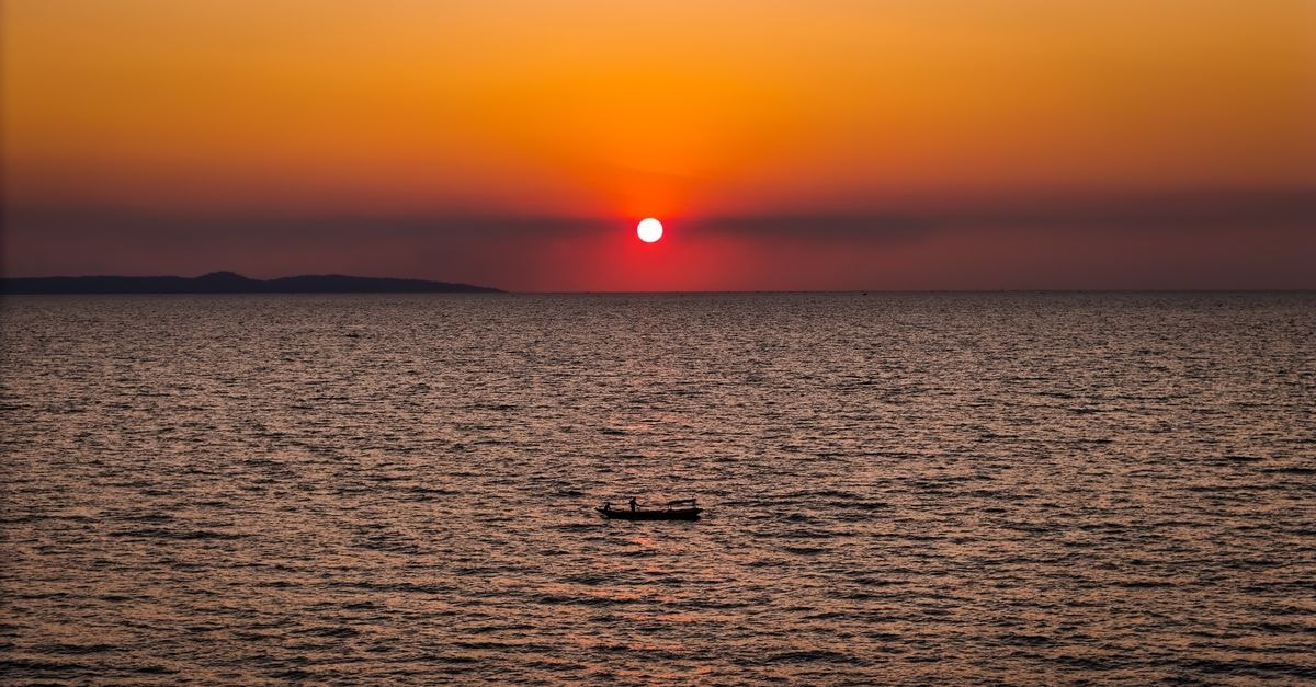 Debitos Hotel in Kupang: A Strategic Stop on Jalan Frans-Seda A serene sunset over the ocean in Kupang, Indonesia, with a lone boat silhouetted.