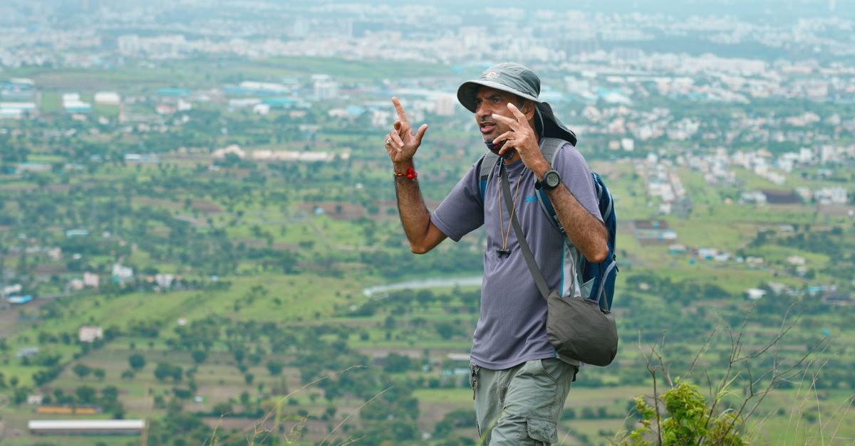 Pimpri-Chinchwad Travel Guide: Getting Around and Eating Well Man on a hike with a beautiful view of Pune city in the background, showcasing adventure and nature.