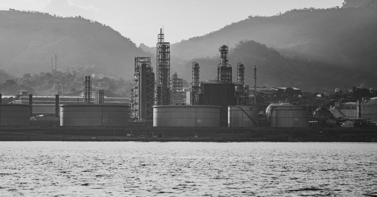 Inox Clean Energy completes ₹6,000 crore acquisition of BlackRock-owned GIP's Vena Energy India A monochrome shot of an industrial refinery near mountains, highlighting its structures.