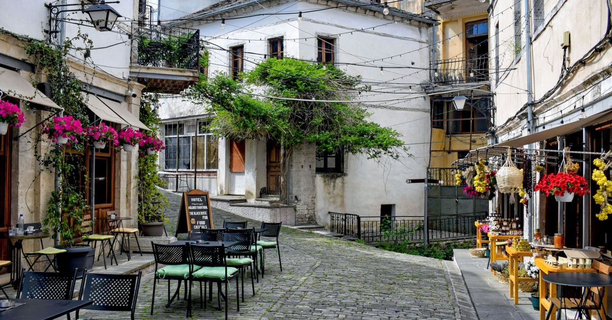 Gjirokastër Travel Guide: Planning Tips, Costs and Things to Do Discover a picturesque street in Gjirokastër, Albania, featuring cozy outdoor cafes and vibrant plants.