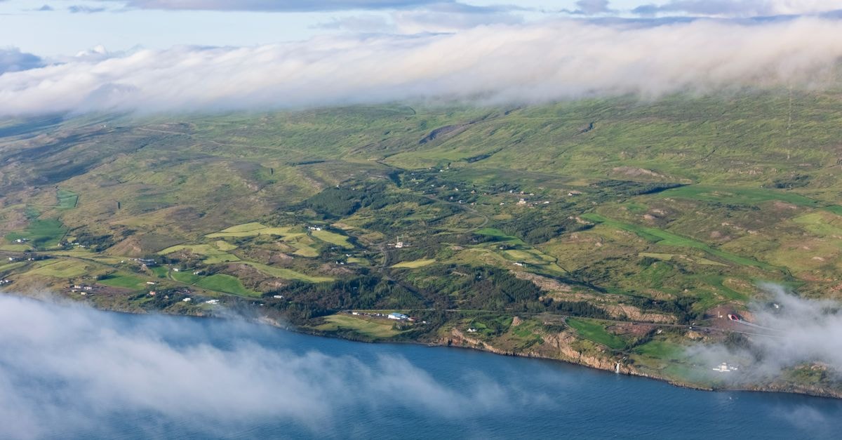 Stunning aerial view of Akureyri, Iceland, featuring mountains, forests, and misty clouds over the coastline.
