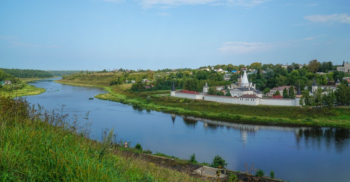 Tyumen Travel Guide: Planning Tips, Costs and Things to Do A peaceful riverside view featuring a historic monastery surrounded by lush greenery under a clear sky.
