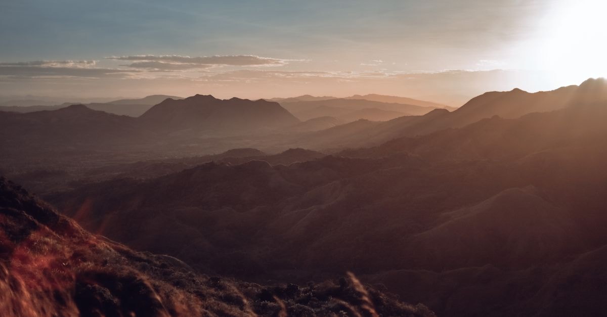 A breathtaking view of mountains during sunrise, showcasing misty valleys and a warm, earthy glow.