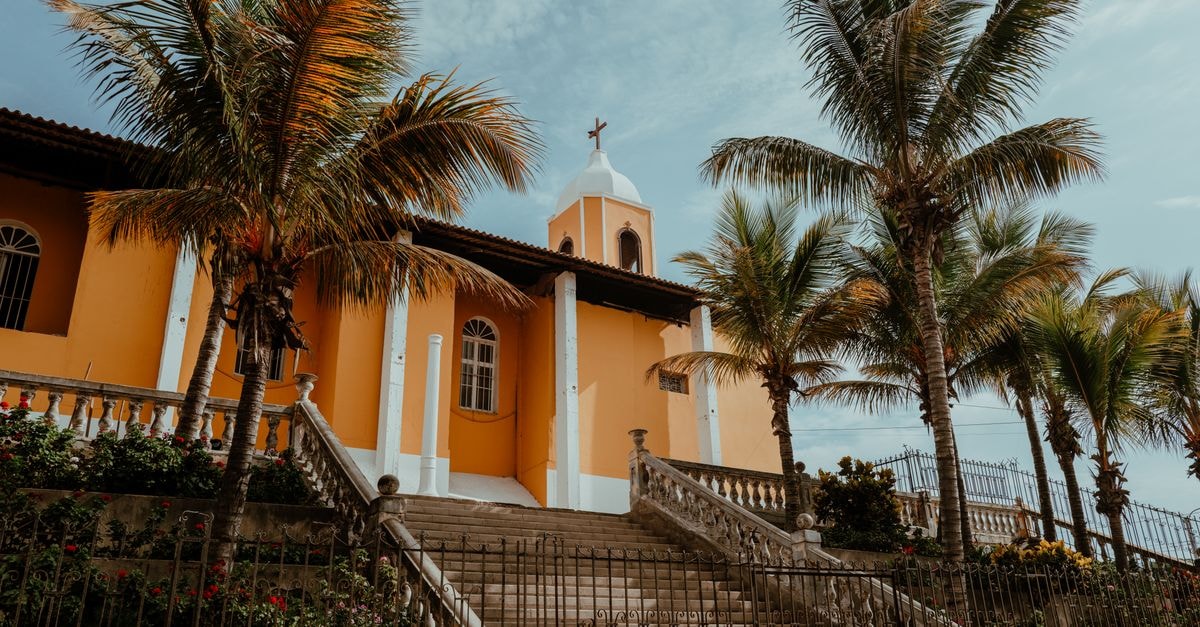 A vibrant church in Pacasmayo, Peru, surrounded by lush palm trees under a clear sky.