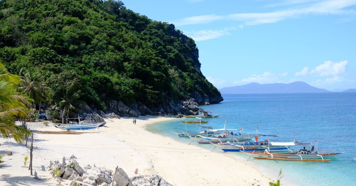 Abakan Travel Guide: Planning Tips, Costs and Things to Do Idyllic tropical beach scene with docked boats, sandy shore, and lush green hills.