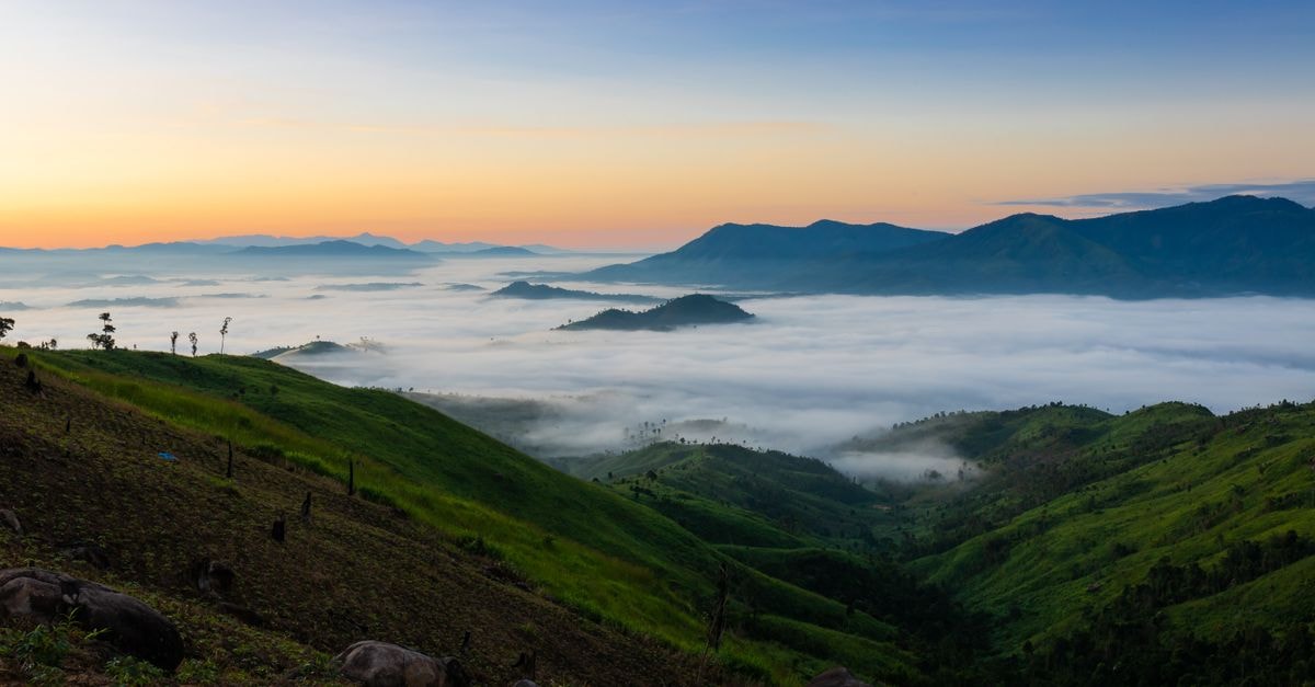 A stunning view of sunrise with mist over lush green mountains in Kon Tum, Vietnam.