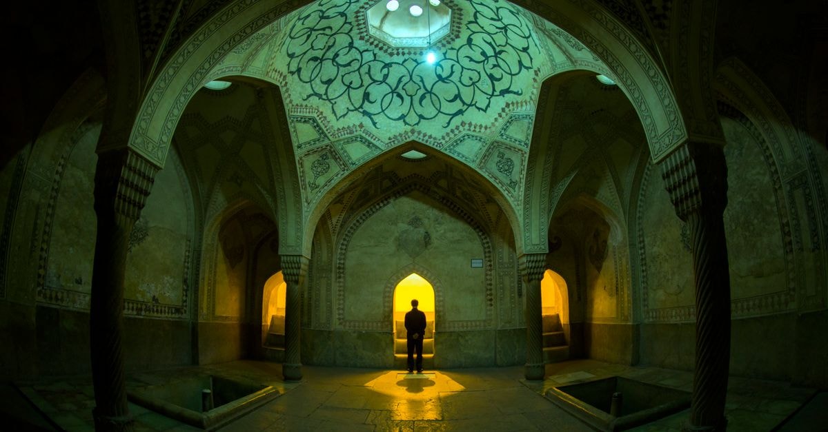 Niayesh Boutique Hotel in Shiraz: A Living Museum of Old Architecture Captivating interior of a historic building in Shiraz, Iran featuring intricate design and a lone figure.