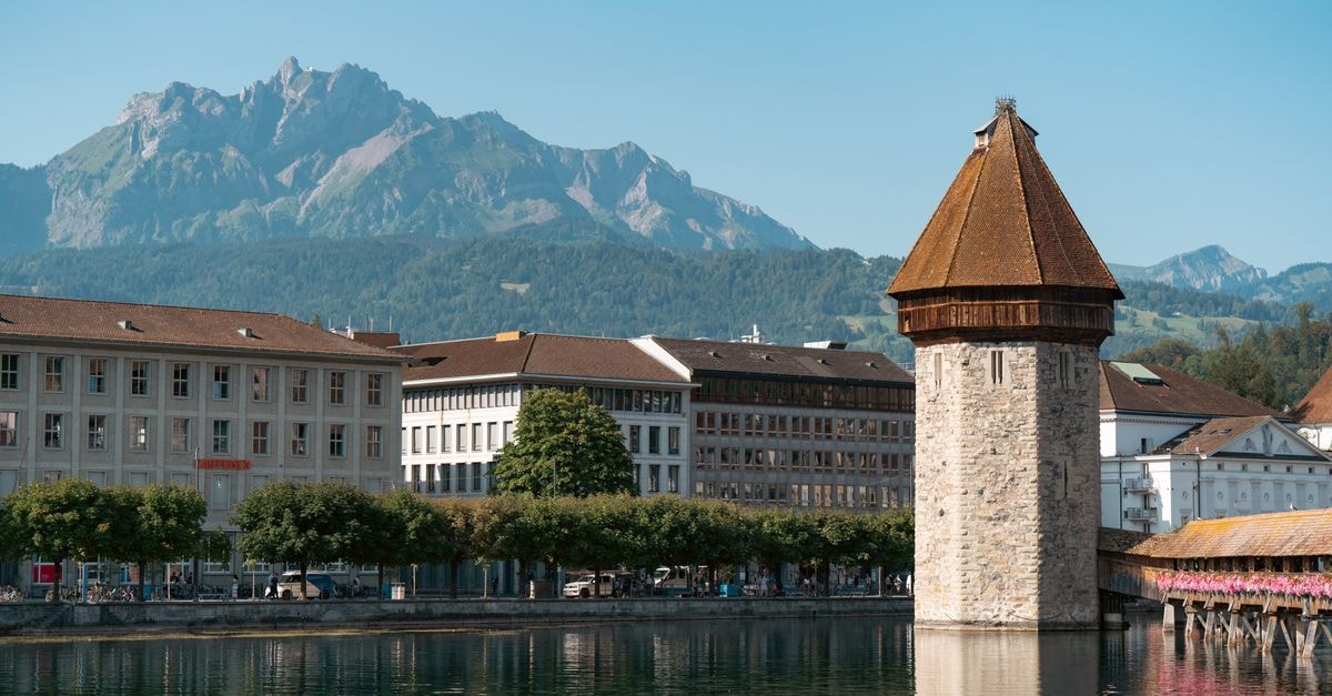Hotel des Balances in Lucerne: A Heritage Riverside Stay in a 12th-Century House Scenic view of Chapel Bridge and Water Tower in Lucerne, Switzerland, with mountains in the background.