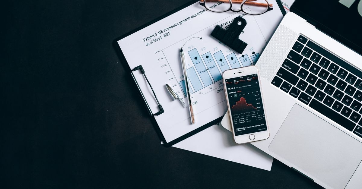 High angle view of an office desk with laptop, clipboard, and smartphone displaying stock market data.