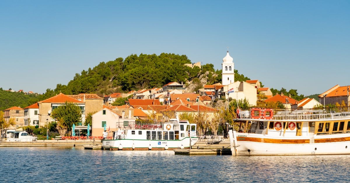 Picturesque view of Skradin harbor with boats and church under a clear summer sky.