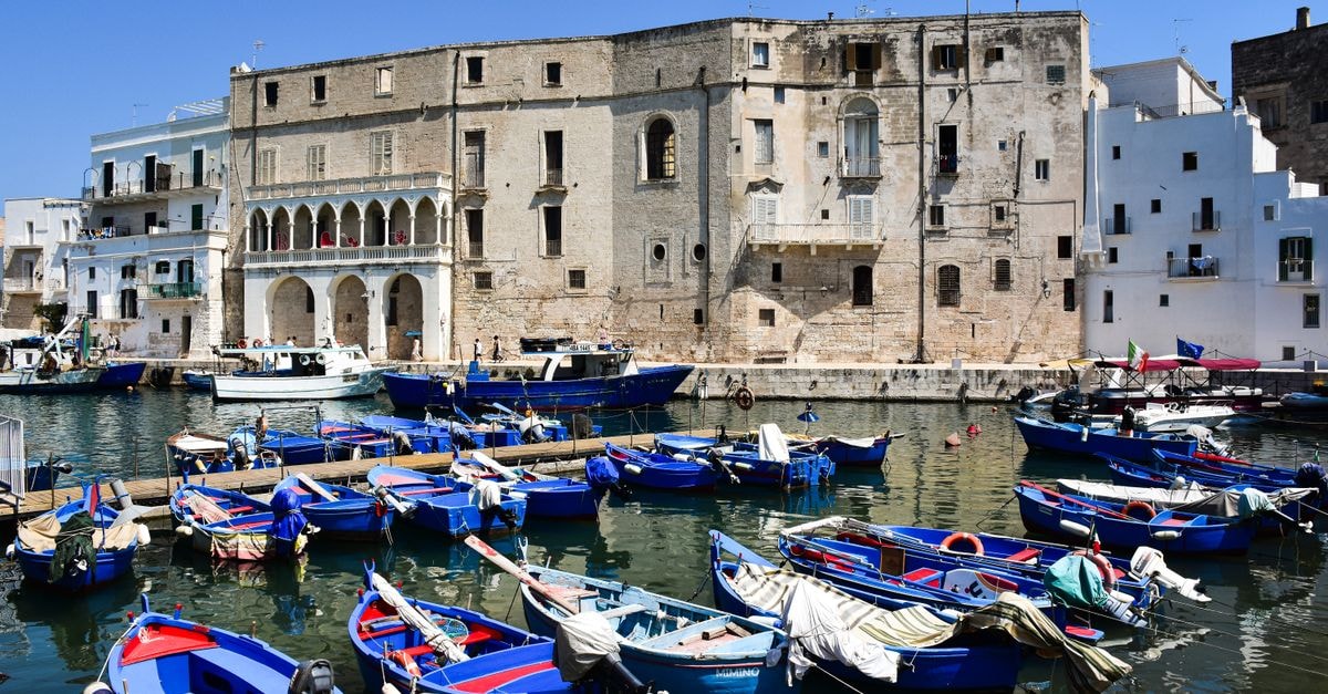 Colorful fishing boats float on a sunny day in the historic harbor of Monopoli, Apulia, Italy.