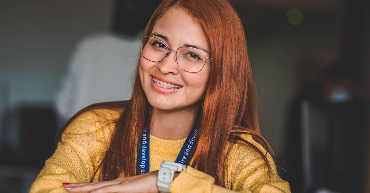 Portrait of a red-haired woman wearing glasses, smiling indoors.
