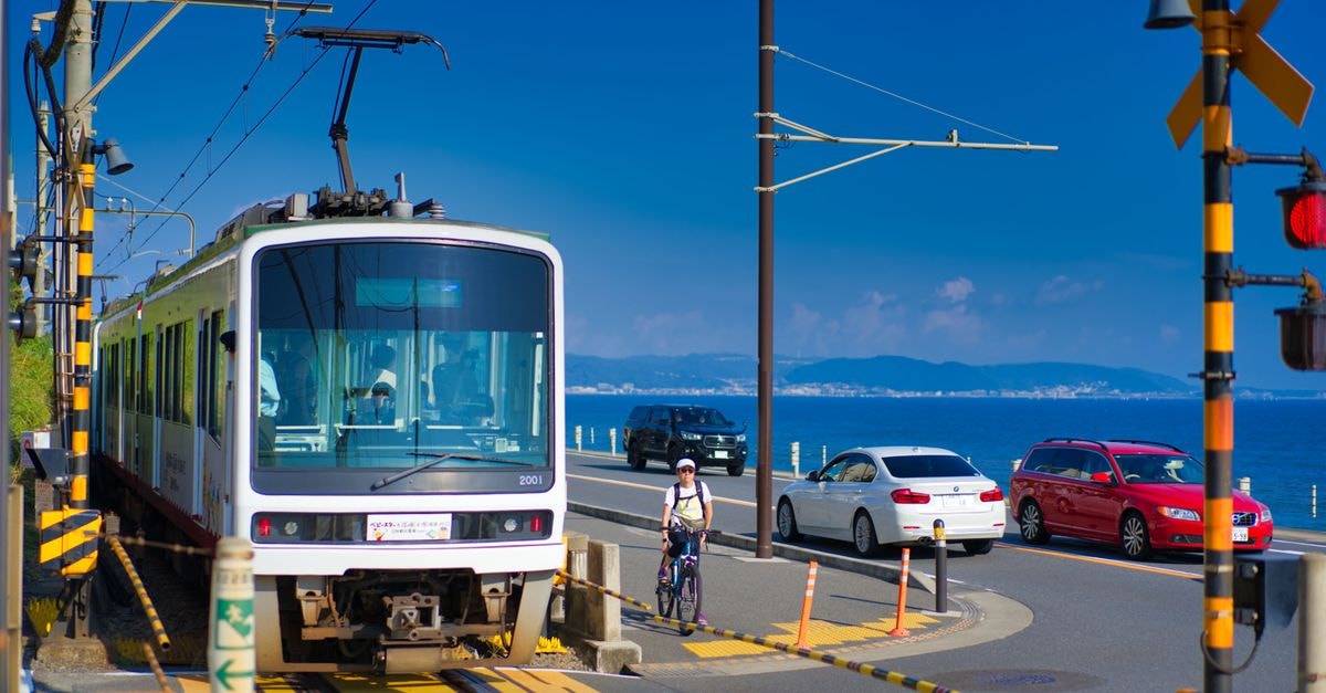 Fujisawa Travel Guide: Slow Days Along the Shonan Coast A vibrant scene of a tram crossing by the coast in Kamakura, Japan, with cyclists and cars nearby.