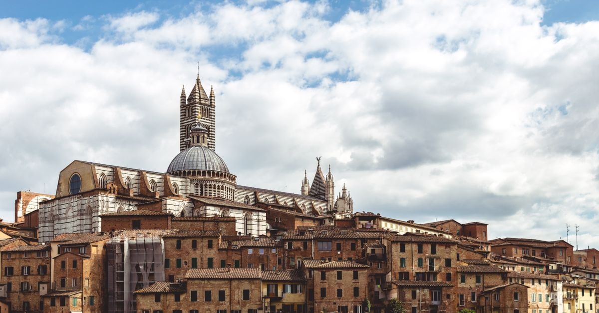 A scenic view of Siena's historic cityscape featuring the iconic Siena Cathedral under a cloudy sky in Tuscany, Italy.