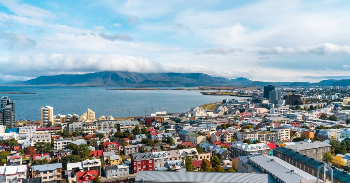 Guesthouse 1×6 in Keflavík: An Art-Filled Stay on Reykjanes Aerial view of Reykjavik, Iceland featuring colorful buildings and ocean vistas under a partly cloudy sky.