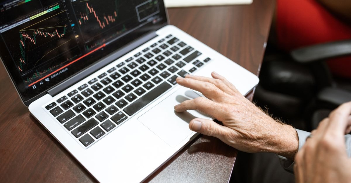 Close-up of hand using laptop for stock market analysis in office setting.