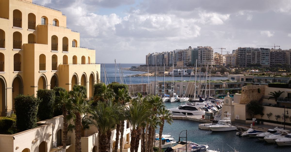 Hilton Malta in St. Julian's: Marina-Side Portomaso Address Scenic view of Hilton Malta's marina with yachts and palm trees, capturing urban luxury by the sea.