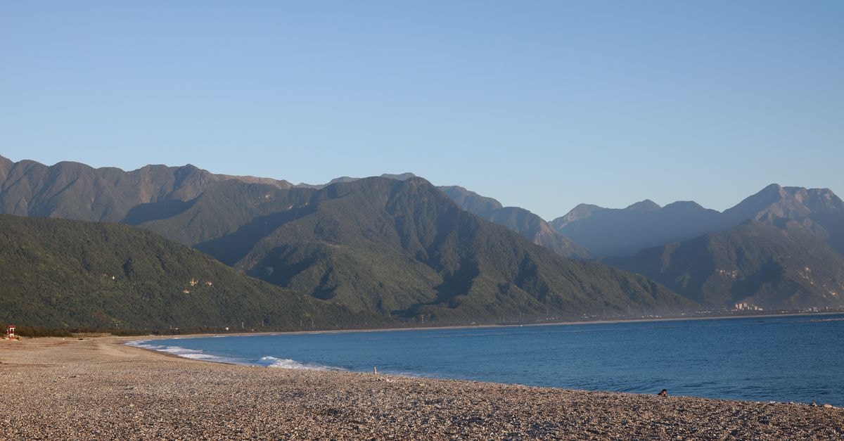 A tranquil pebble beach in Taiwan, framed by mountains and a clear blue sky.