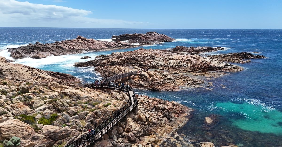 Explore the scenic coastline of Western Australia with rugged rocks, clear blue sea, and a vibrant walkway.