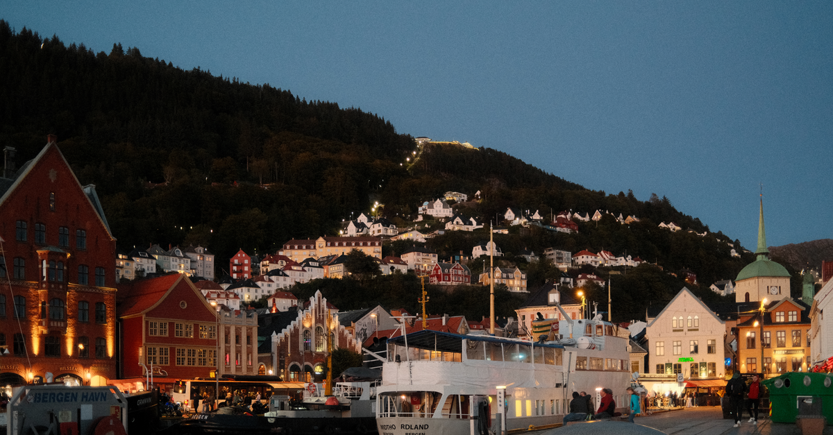 A Slow-Travel Guide to Bergen, Norway's Rain-Kissed Harbor City Scenic evening view of Bergen's iconic Bryggen waterfront with lit buildings and boats.