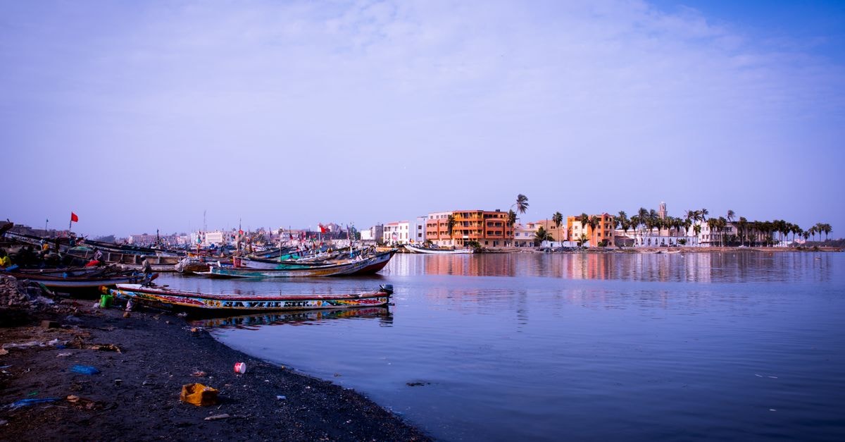 Peaceful coastline scene with moored boats and distant colorful buildings under a clear sky.