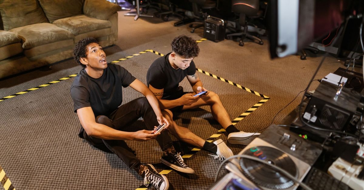 Two friends sitting on the floor playing video games indoors with controllers and enjoying the leisure time.
