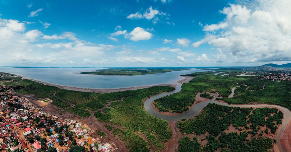 Brazzaville Travel Guide: River-Light Discoveries on the Congo Panoramic aerial view of a coastal city with lush greenery, winding river, and expansive blue sky.