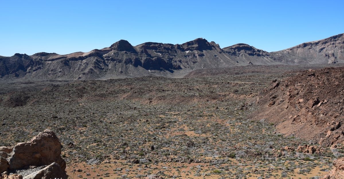 Expansive desert landscape with rugged mountains under a clear blue sky.