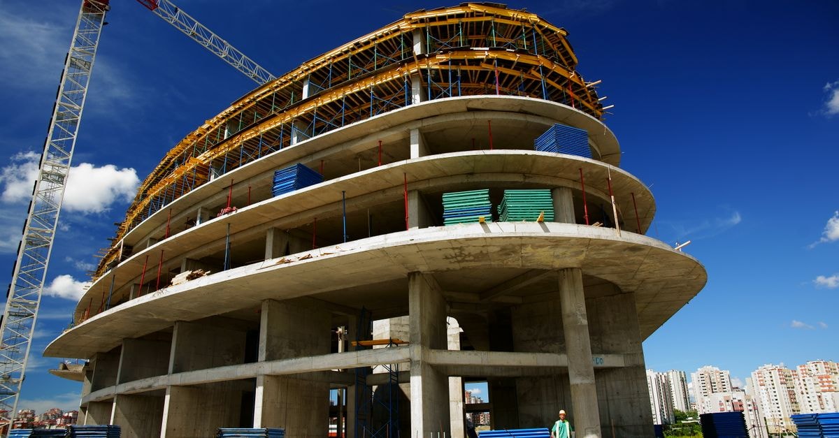 Low angle view of a circular building under construction with a crane, clear blue sky.