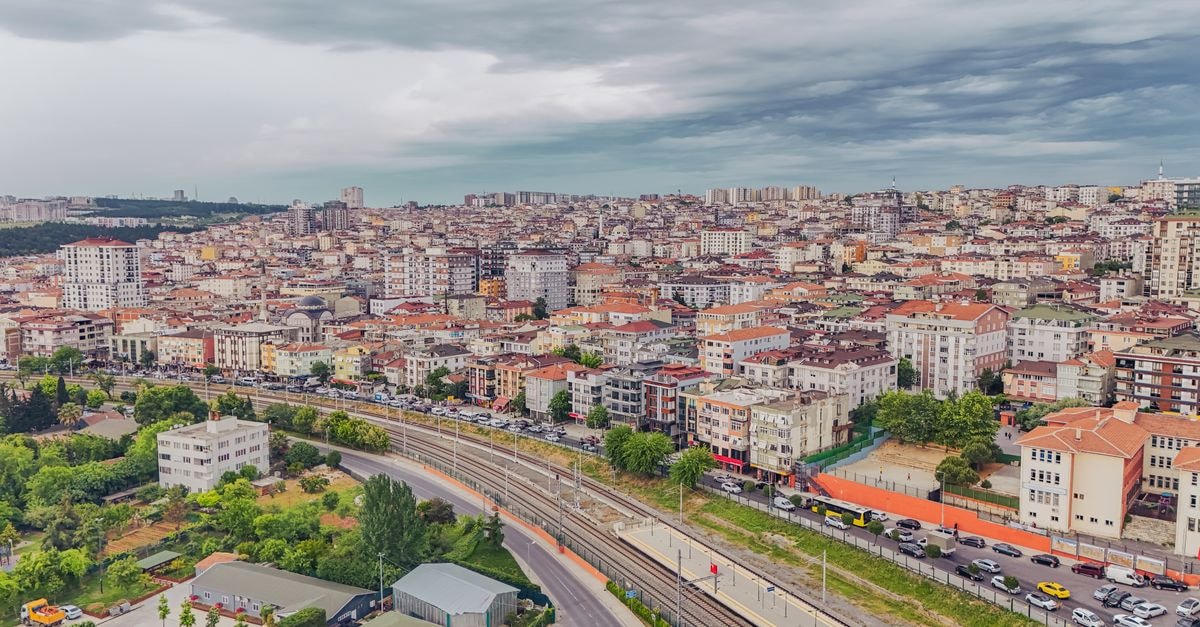 Aerial view of dense urban architecture with roads and greenery under cloudy skies.