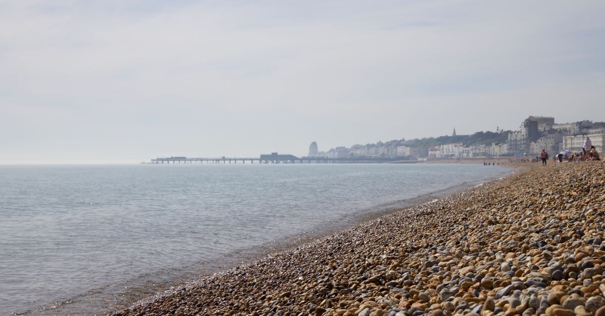 Serene pebble beach with a view of a distant pier and coastal city skyline, perfect for a summer day.
