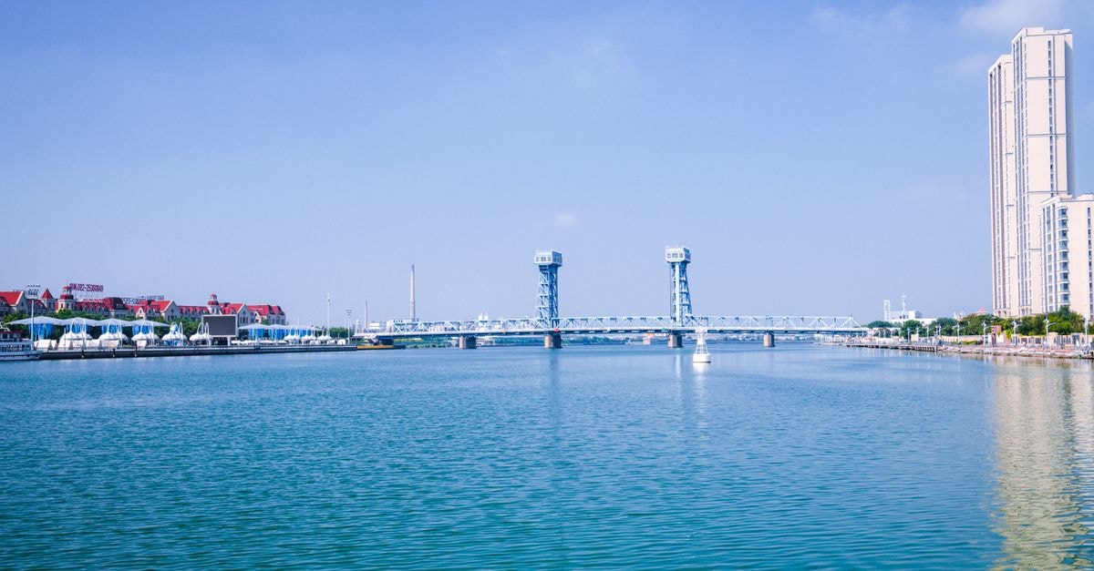 Scenic urban waterfront view with a bridge and skyscrapers reflecting on calm blue water.