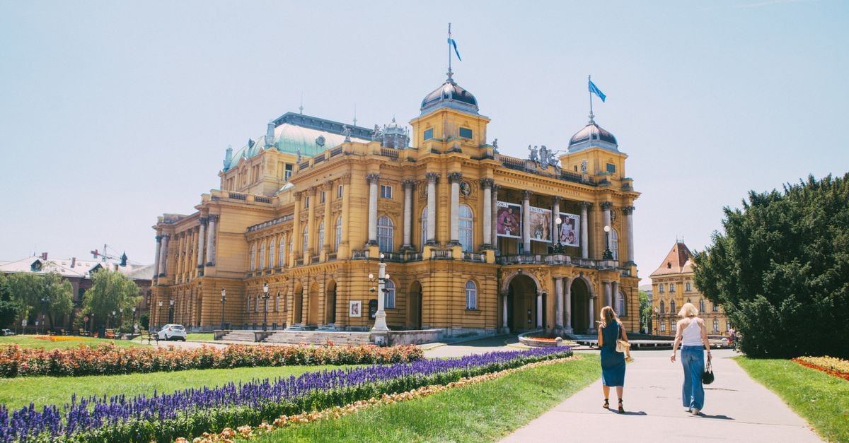 Hostel Bureau, Zagreb — 24-Hour Reception Steps from the Old Town A sunny day view of the Croatian National Theatre with flowerbeds and people walking.