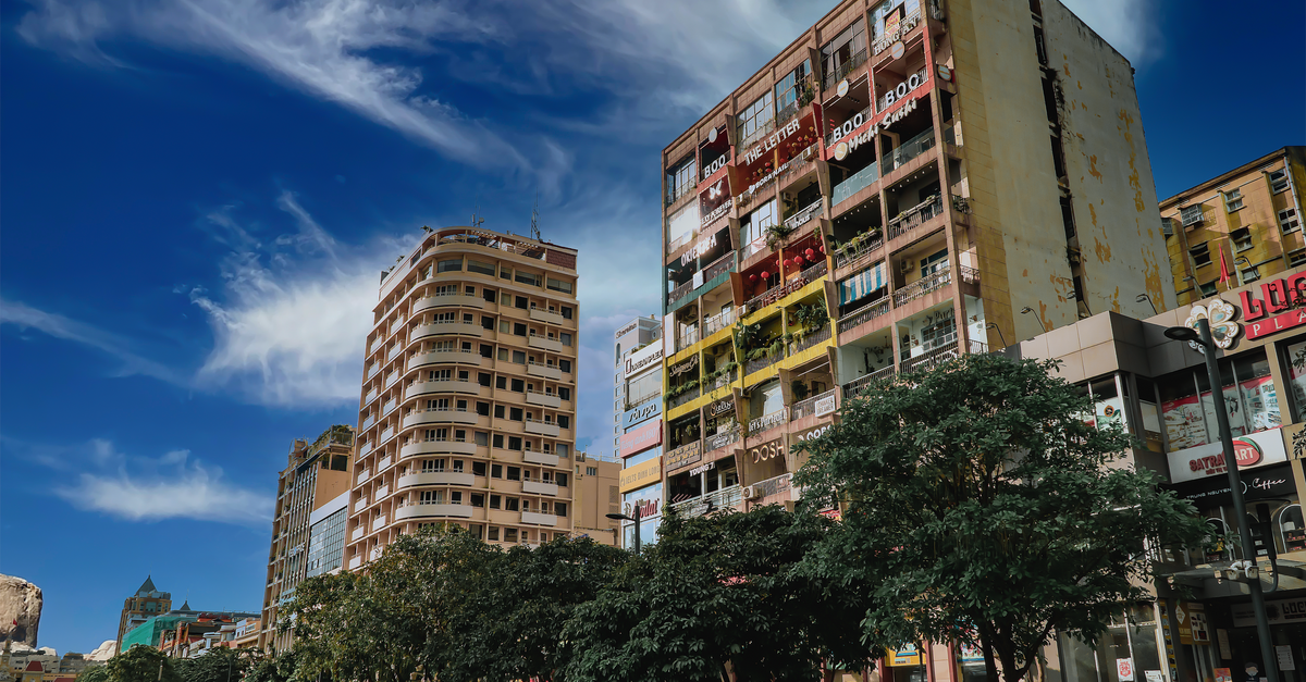 Cityscape view featuring tall buildings, trees, and a vibrant blue sky.