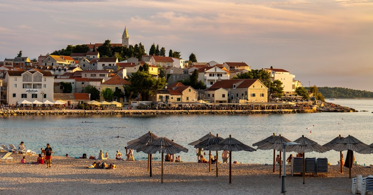 Beautiful beach scene with town and umbrellas at sunset in Primošten, Croatia.