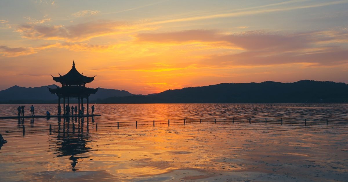 Taizhou Travel Guide: Mountains, Waterways, and a Slower Zhejiang Rhythm Silhouettes at West Lake in Hangzhou during a serene sunset with a traditional pagoda view.