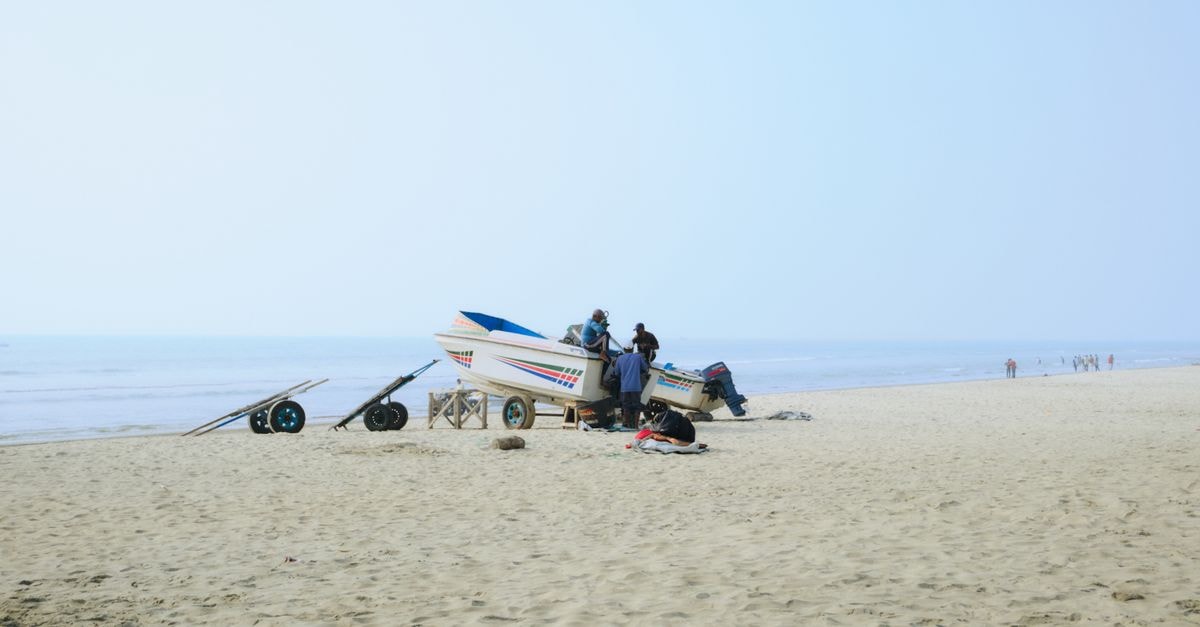 Cox's Bazar Travel Guide: Getting There and Finding Your Beach Day Fishermen with a boat on the sandy shores of Cox's Bazar beach under a clear blue sky.