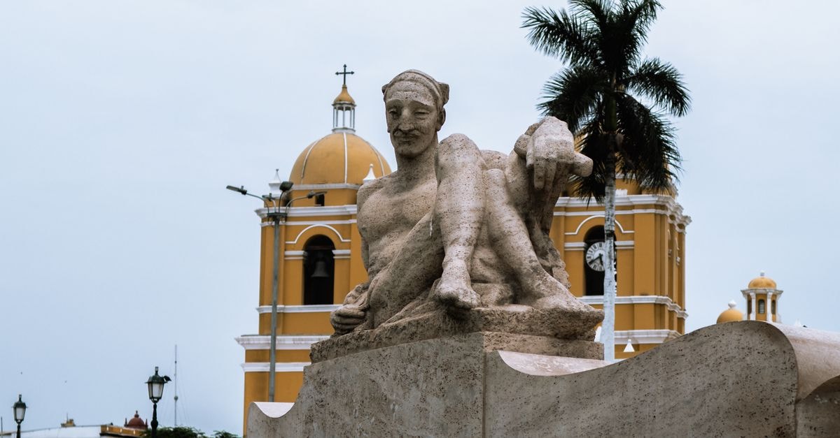 The Plaza de Armas in Trujillo, Peru, featuring a prominent sculpture and colonial architecture under a cloudy sky.