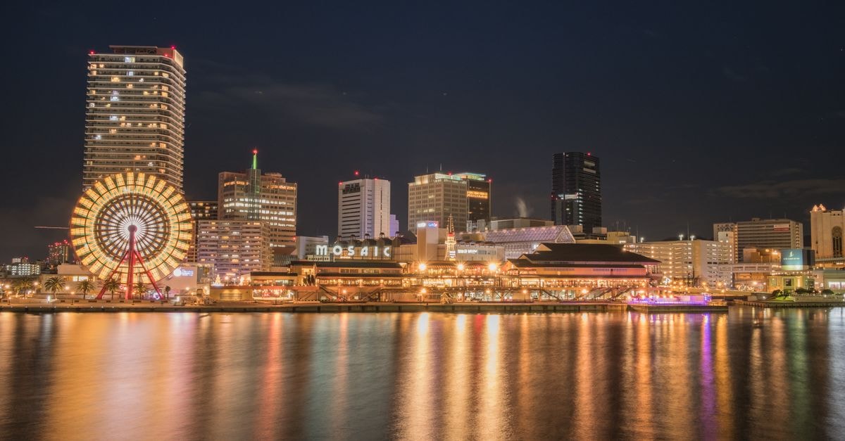Stunning night cityscape of Kobe with illuminated Ferris wheel reflecting on the waterfront.