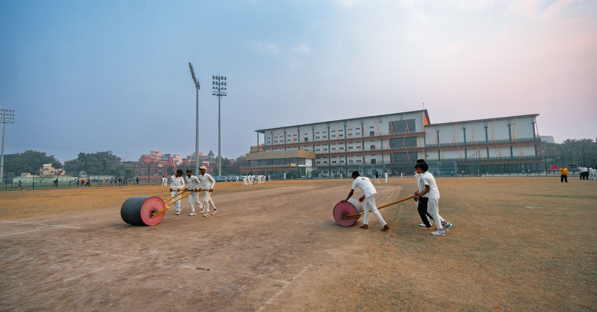 Groundskeepers preparing cricket field in Delhi, India with rollers at sunset.