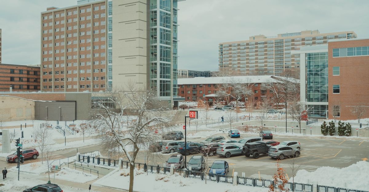 Kimpton Journeyman Hotel in Milwaukee: Rooftop Bar and Third Ward Brick Snow-covered urban scene with Milwaukee campus buildings and parking lot in winter.