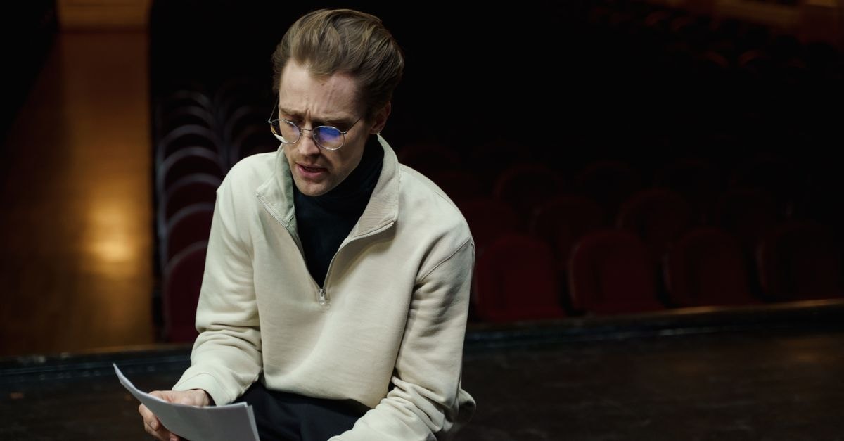 An actor rehearses lines on a theater stage, conveying focus and dedication in a dimly lit setting.