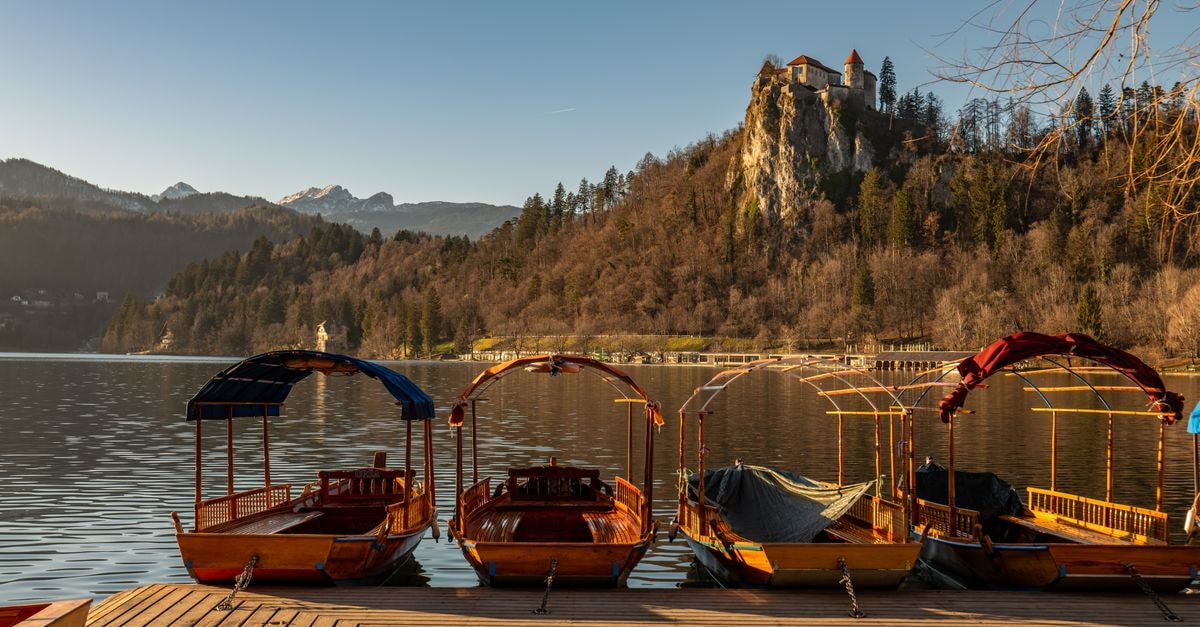 Bled travel guide: castle views, calm lake mornings Scenic view of Lake Bled and castle with four pletna boats in Slovenia.