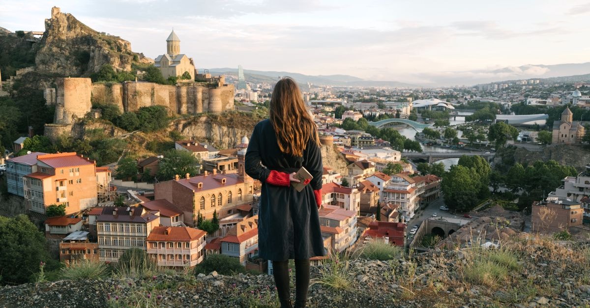 Kabarnet Travel Guide: Planning Tips, Costs and Things to Do Woman overlooks Tbilisi cityscape with historic fortress and churches under a pastel sky.