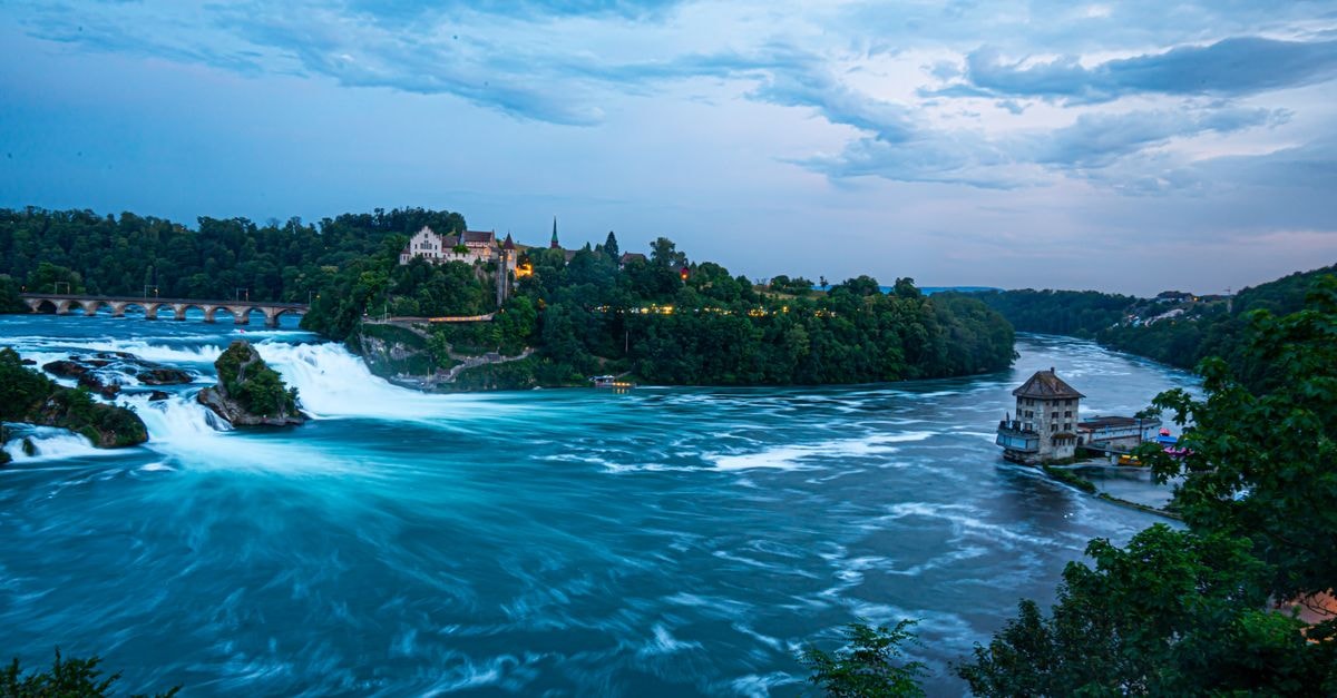 A stunning view of the Rhine Falls with vibrant blue waters at twilight in Schaffhausen, Switzerland.