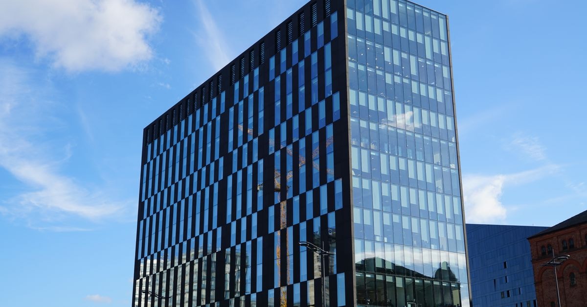 Gatik raises $200M to scale driverless middle-mile delivery after PepsiCo deal Tall glass office building reflecting blue sky with scattered clouds.