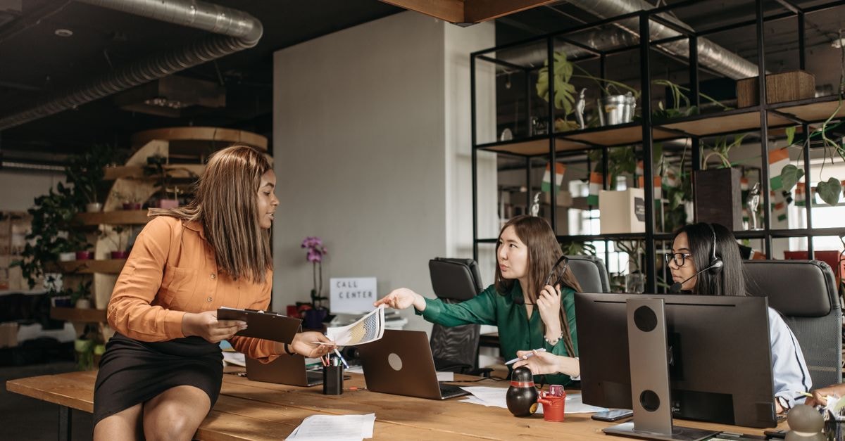 ManpowerGroup: Cyclical Engine at a Premium Price Diverse group of female professionals discussing work at their desk in a modern office setting.