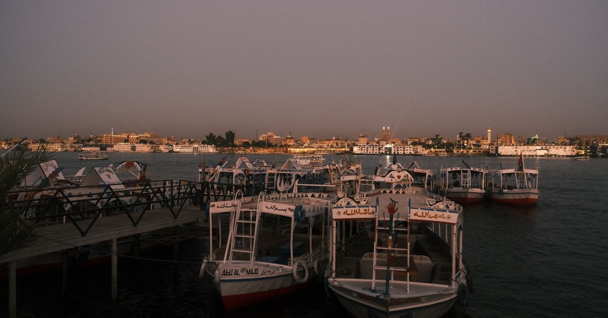 Boats docked on the Nile River in Luxor at sunset, capturing a tranquil evening scene.