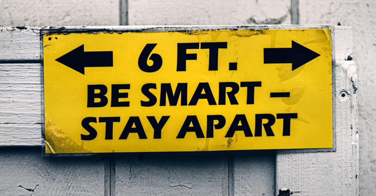 Yellow sign urging social distancing with 'Be Smart, Stay Apart' message on wood.